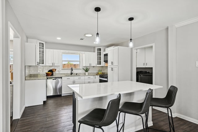 kitchen featuring dark wood-type flooring, stove, a sink, stainless steel dishwasher, and a kitchen bar