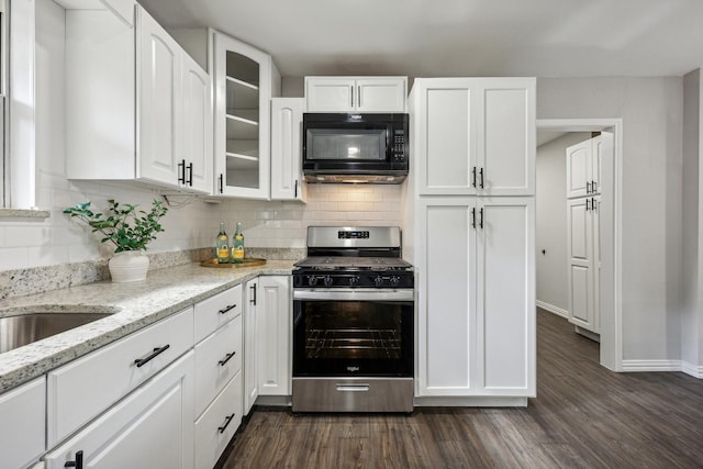 kitchen featuring black microwave, stainless steel gas range oven, dark wood-type flooring, white cabinetry, and decorative backsplash