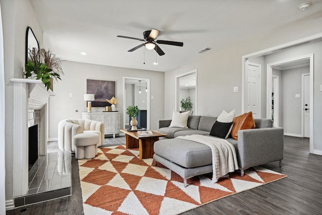 living area with baseboards, visible vents, a fireplace with raised hearth, ceiling fan, and dark wood-type flooring