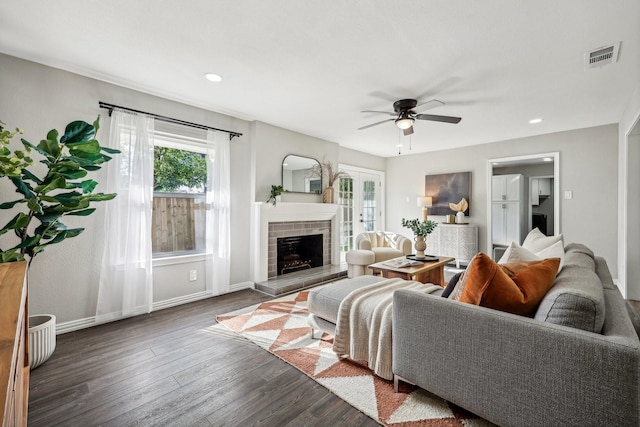 living room with a fireplace, visible vents, dark wood-type flooring, ceiling fan, and baseboards