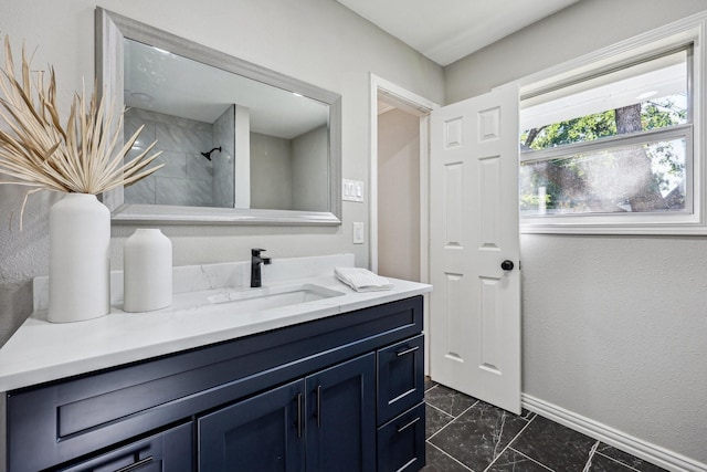 full bath with baseboards, tiled shower, and vanity