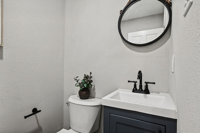 bathroom with a textured wall, vanity, and toilet