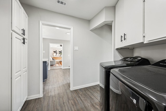 clothes washing area with washer and clothes dryer, visible vents, cabinet space, dark wood-type flooring, and baseboards