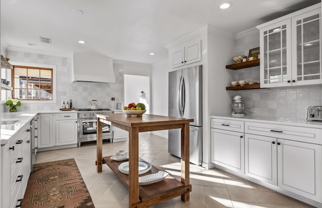 kitchen with premium range hood, appliances with stainless steel finishes, white cabinets, light tile patterned floors, and crown molding