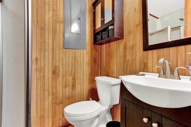 bathroom featuring toilet, wood walls, electric panel, and vanity