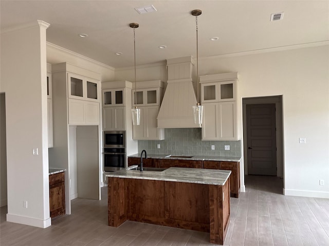 kitchen featuring a sink, custom range hood, white cabinets, appliances with stainless steel finishes, and backsplash