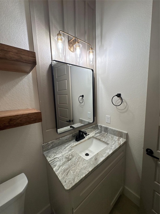 half bath featuring toilet, vanity, and a textured wall