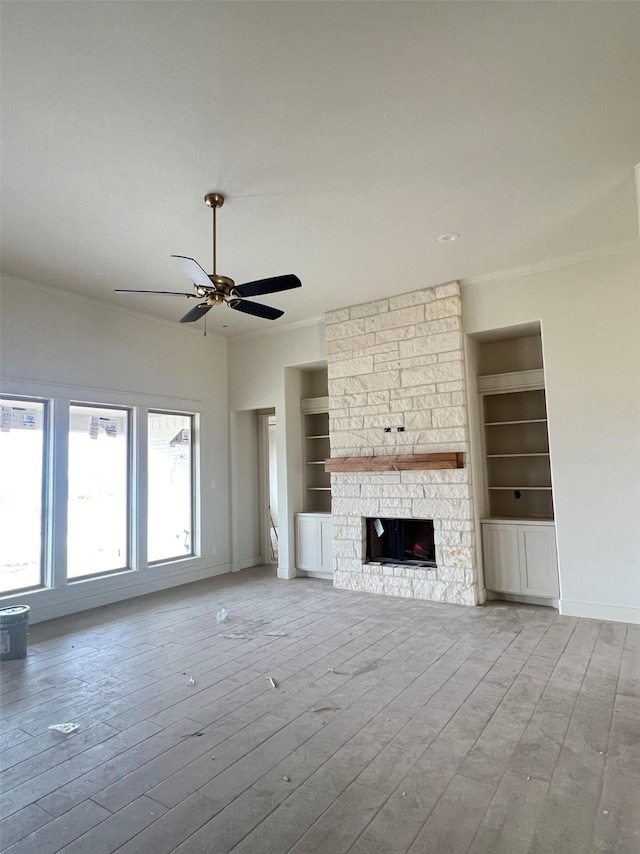 unfurnished living room with built in shelves, a stone fireplace, and light wood-type flooring