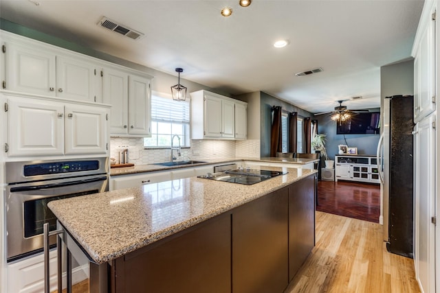 kitchen with a kitchen island, appliances with stainless steel finishes, pendant lighting, white cabinetry, and sink