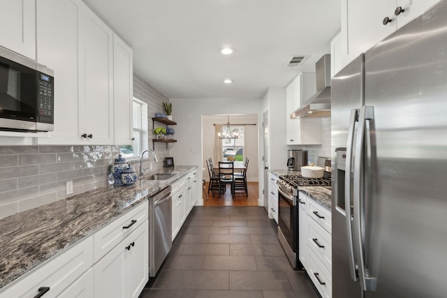 kitchen with sink, appliances with stainless steel finishes, white cabinets, wall chimney range hood, and backsplash