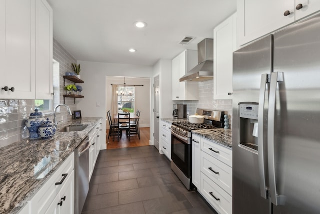 kitchen featuring sink, stone countertops, wall chimney range hood, stainless steel appliances, and white cabinets