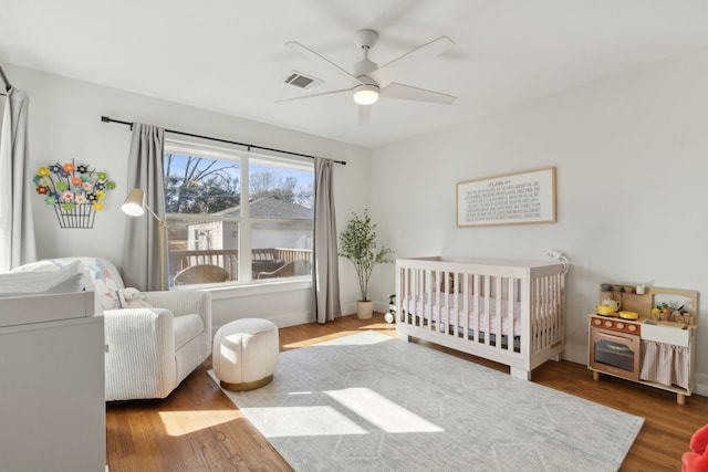 bedroom featuring a nursery area, ceiling fan, and wood-type flooring