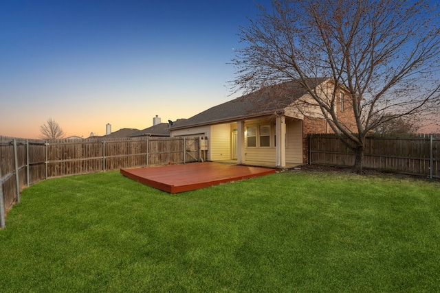 back house at dusk with a wooden deck and a lawn