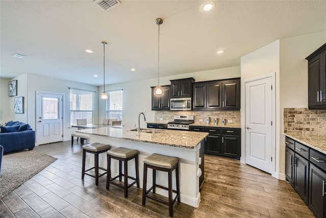 kitchen with sink, stainless steel appliances, an island with sink, a kitchen bar, and decorative light fixtures