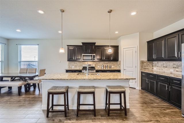 kitchen with hanging light fixtures, a center island with sink, sink, and appliances with stainless steel finishes