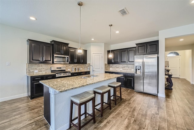 kitchen featuring appliances with stainless steel finishes, an island with sink, sink, a breakfast bar area, and light stone countertops