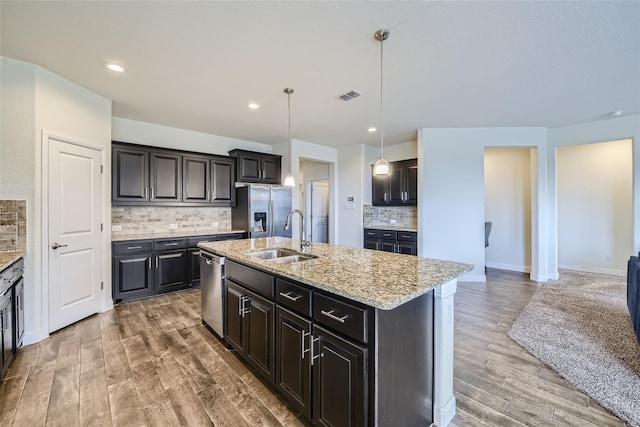 kitchen with sink, hardwood / wood-style flooring, appliances with stainless steel finishes, pendant lighting, and a kitchen island with sink