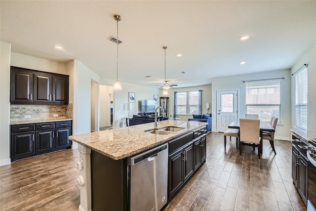 kitchen with sink, dishwasher, a kitchen island with sink, hanging light fixtures, and dark hardwood / wood-style flooring