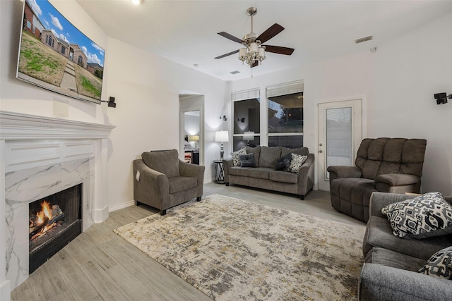 living room with a high end fireplace, ceiling fan, and light wood-type flooring