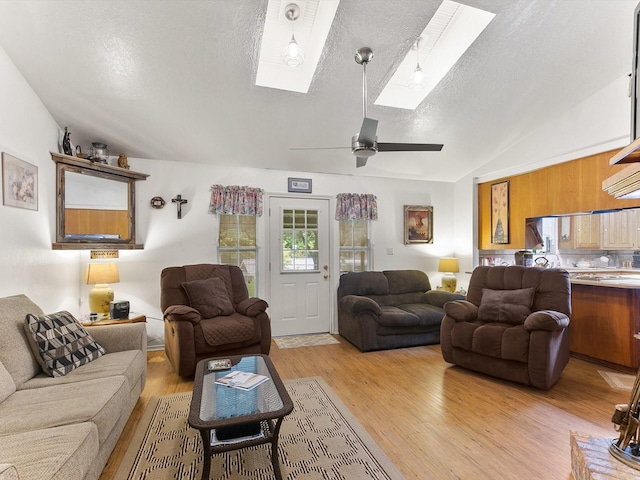 living room with lofted ceiling with skylight, ceiling fan, a textured ceiling, and light hardwood / wood-style flooring