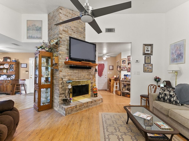 living room with hardwood / wood-style floors, a towering ceiling, a brick fireplace, and ceiling fan