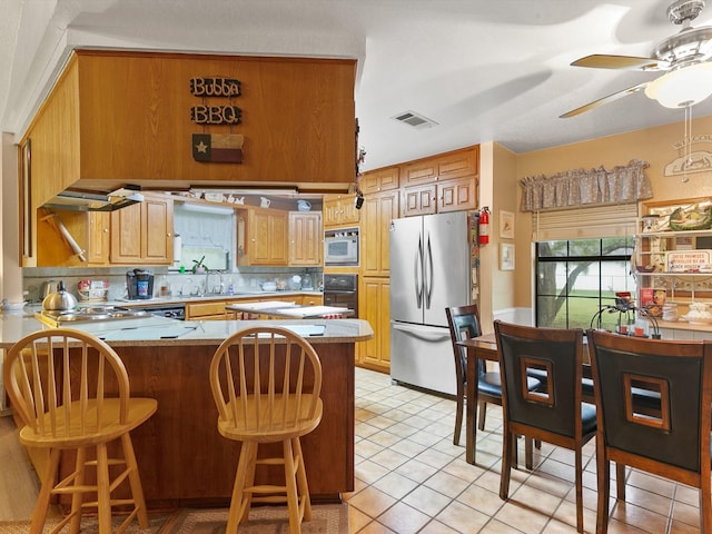 kitchen with appliances with stainless steel finishes, a breakfast bar area, decorative backsplash, ceiling fan, and kitchen peninsula