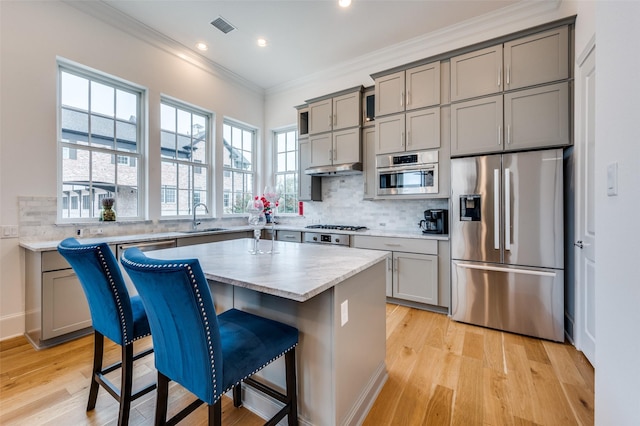 kitchen with a kitchen island, a breakfast bar, sink, ornamental molding, and stainless steel appliances