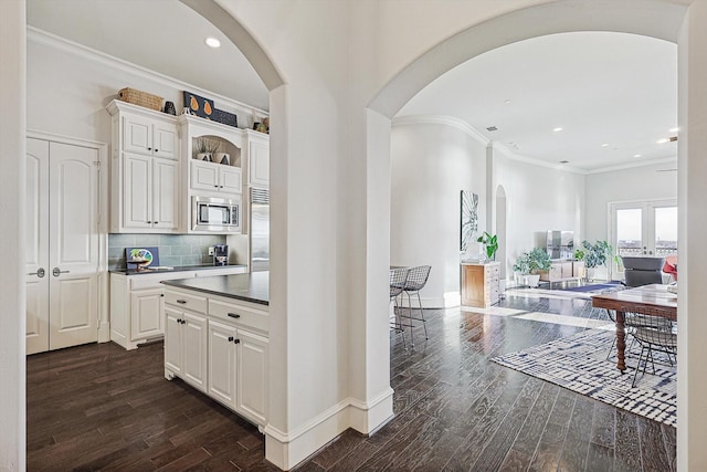 kitchen featuring crown molding, dark wood-type flooring, white cabinetry, backsplash, and stainless steel microwave