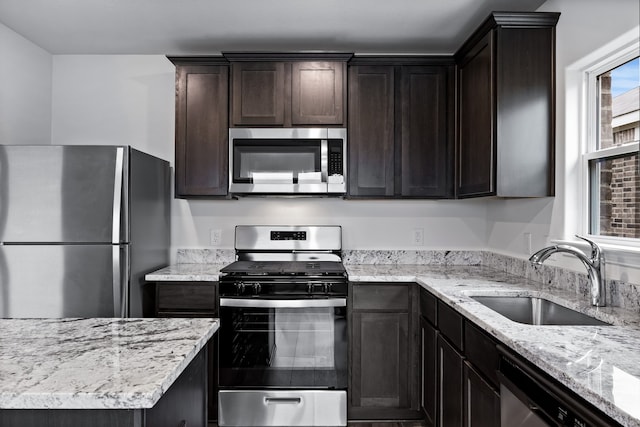 kitchen featuring stainless steel appliances, dark brown cabinets, sink, and light stone counters