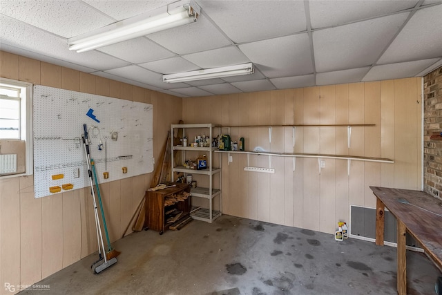 interior space featuring wood walls, a drop ceiling, and a workshop area