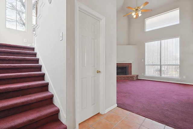 stairway with ceiling fan, a fireplace, carpet floors, and a high ceiling