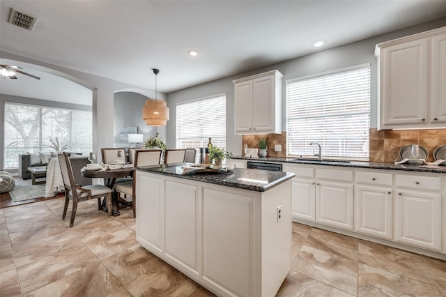 kitchen with sink, hanging light fixtures, white cabinets, a kitchen island, and dark stone counters