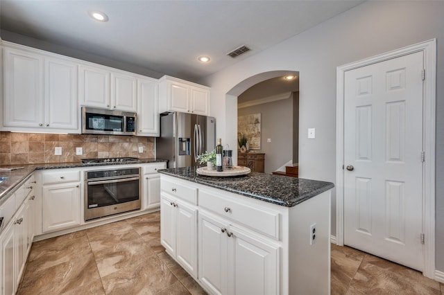 kitchen featuring tasteful backsplash, dark stone countertops, appliances with stainless steel finishes, a kitchen island, and white cabinets