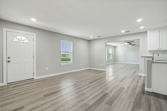 unfurnished living room with sink, ceiling fan, and light wood-type flooring