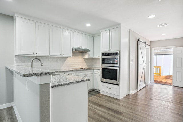 kitchen with white cabinetry, a barn door, kitchen peninsula, and double oven