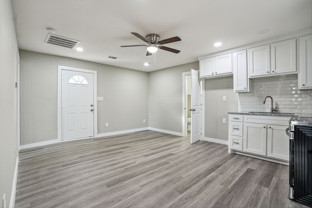 kitchen with tasteful backsplash, white cabinetry, sink, ceiling fan, and light hardwood / wood-style flooring