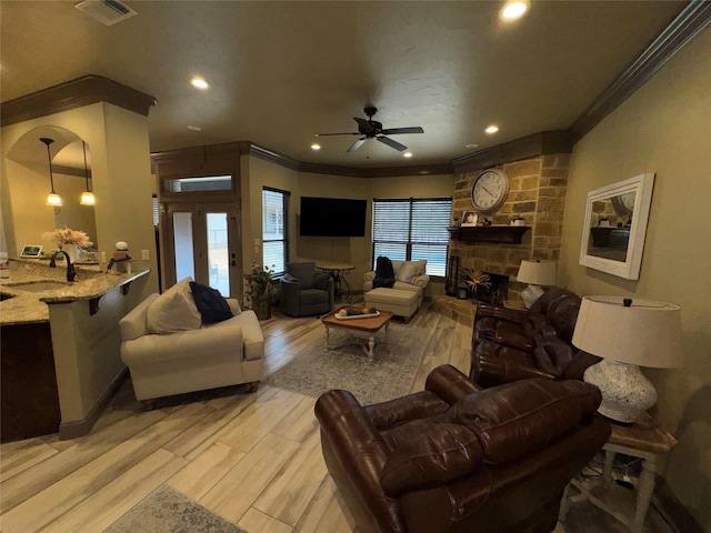 living room with crown molding, a stone fireplace, sink, and light hardwood / wood-style flooring