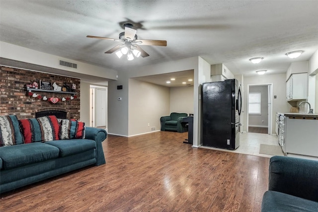 living room with sink, ceiling fan, a fireplace, wood-type flooring, and a textured ceiling