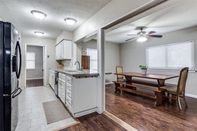 kitchen with wood-type flooring, sink, white cabinets, decorative backsplash, and black fridge