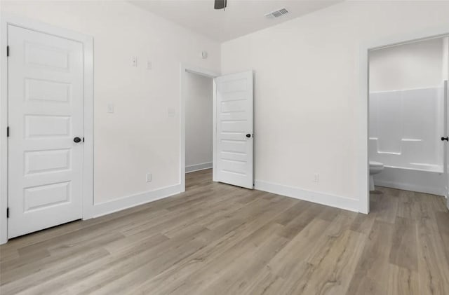 unfurnished bedroom with ceiling fan, ensuite bath, and light wood-type flooring