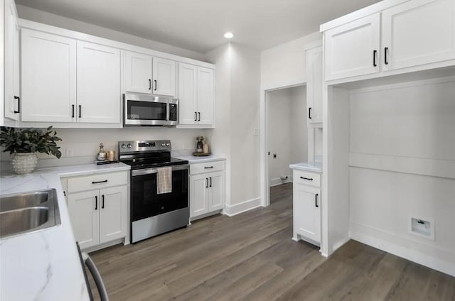 kitchen with sink, white cabinetry, stainless steel appliances, light stone counters, and dark hardwood / wood-style flooring