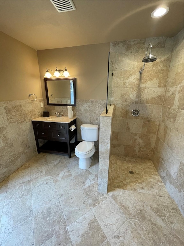 bathroom with vanity, a tile shower, tile walls, and toilet