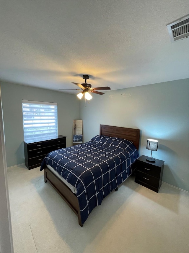 bedroom with ceiling fan, light colored carpet, and a textured ceiling