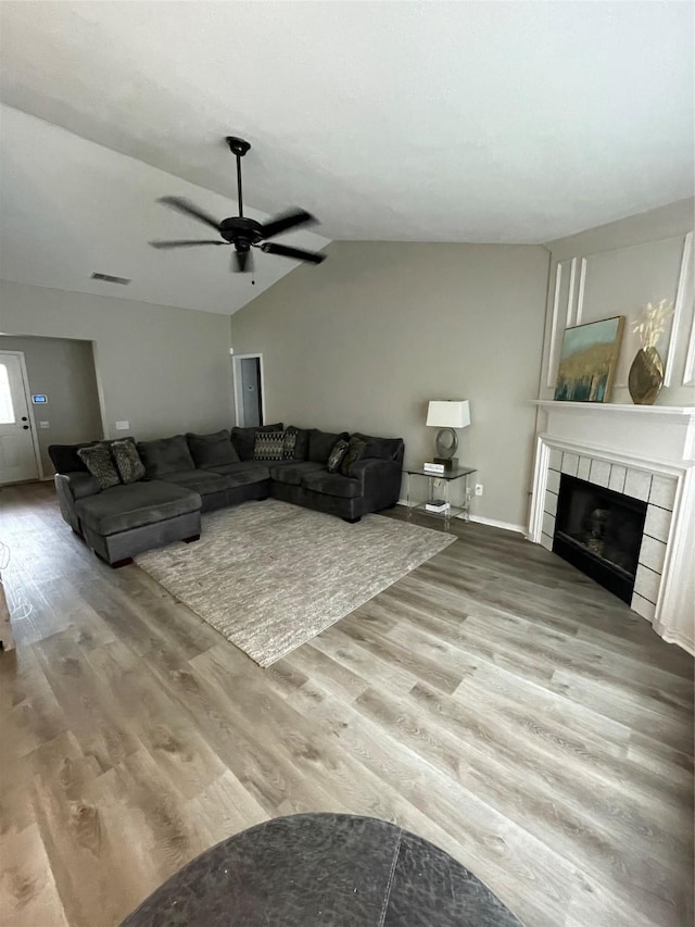 living room with hardwood / wood-style flooring, ceiling fan, lofted ceiling, and a tiled fireplace