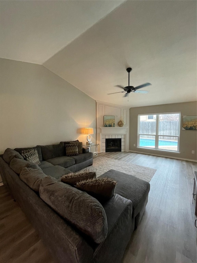 living room with a tiled fireplace, hardwood / wood-style flooring, lofted ceiling, and ceiling fan