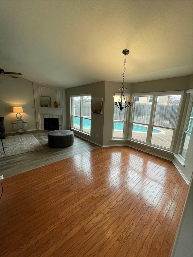 unfurnished living room with hardwood / wood-style flooring, a fireplace, and ceiling fan with notable chandelier