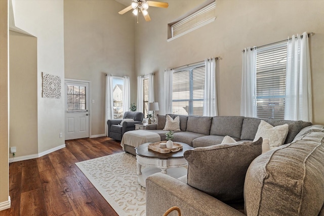 living room with dark wood-type flooring, ceiling fan, and a high ceiling