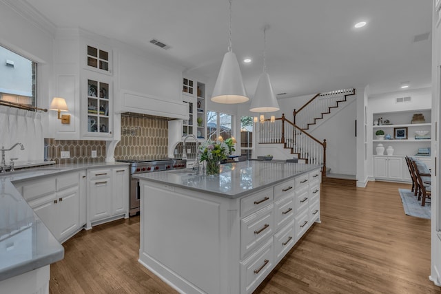 kitchen with sink, white cabinetry, high end stainless steel range, a kitchen island, and decorative light fixtures