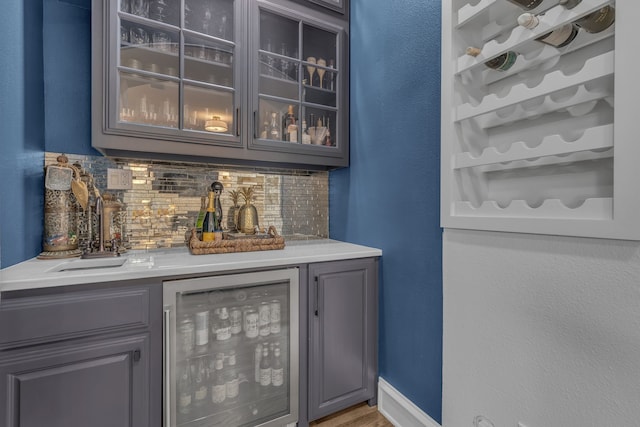 bar featuring gray cabinets, sink, beverage cooler, and backsplash