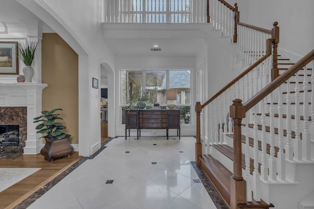 foyer with tile patterned flooring, a towering ceiling, and a high end fireplace